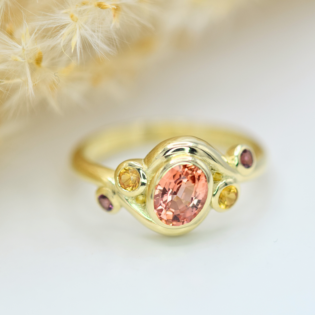 oval peach padparadscha with yellow and purple sapphire side stones in 14k yellow gold chunky ring