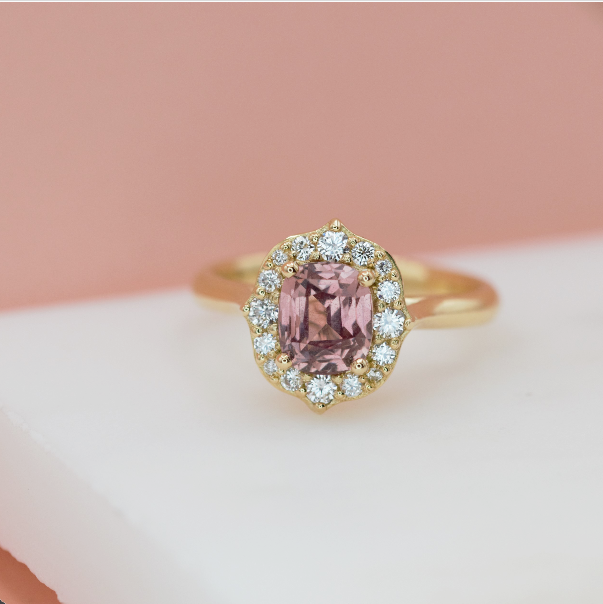 An 18k yellow gold ring featuring a cushion cut champagne sapphire with a halo of round diamonds around it.