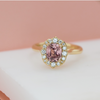 An 18k yellow gold ring featuring a cushion cut champagne sapphire with a halo of round diamonds around it.